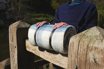 A person placing their hands on top of a rolled up blue and white wool picnic rug. 