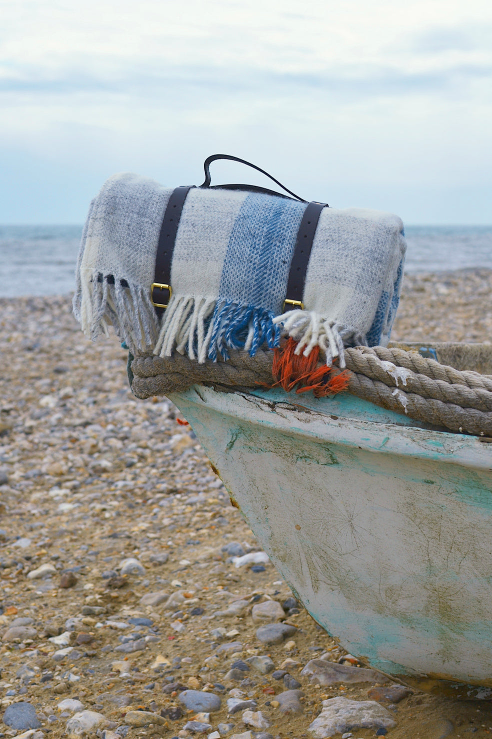 A rolled up blue and white wool picnic rug placed on the edge of a boat. 