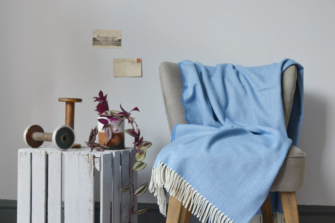 Large blue merino herringbone wool blanket draped over a lounge chair. 