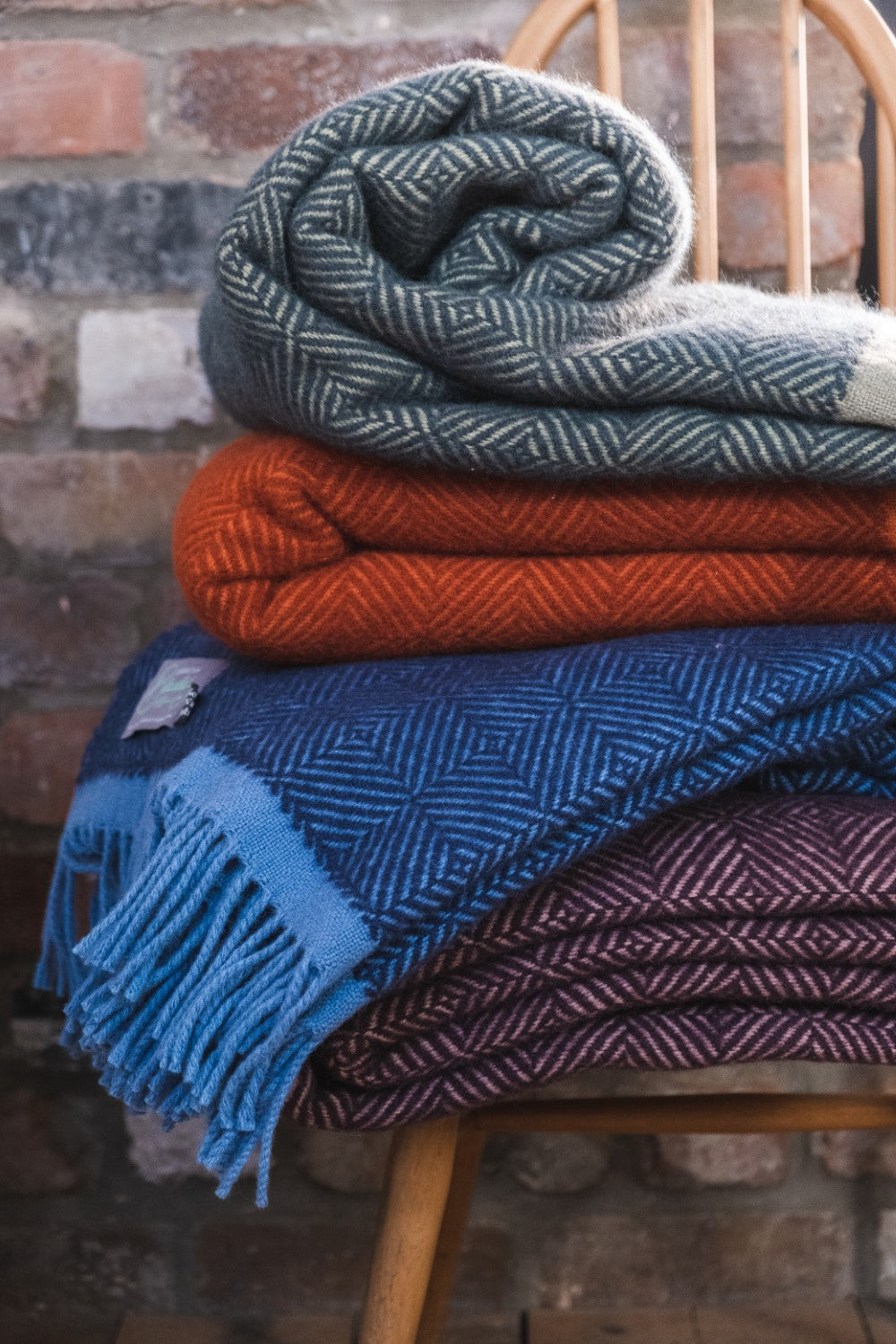 Four wool throws stacked on top of a wooden chair.