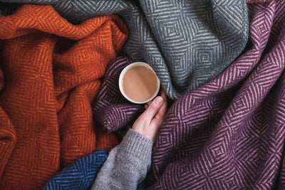 A tea cup being held in the middle of a pile of wool blankets