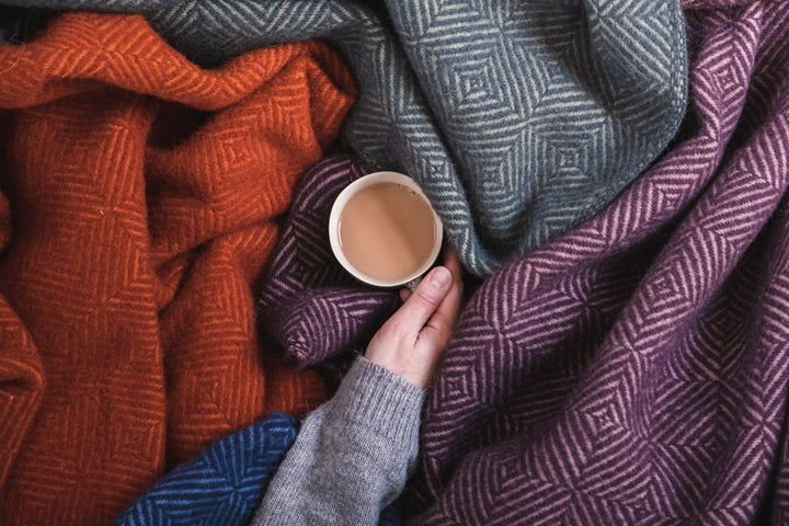 A cup of tea being held in the middle of a pile of wool throws