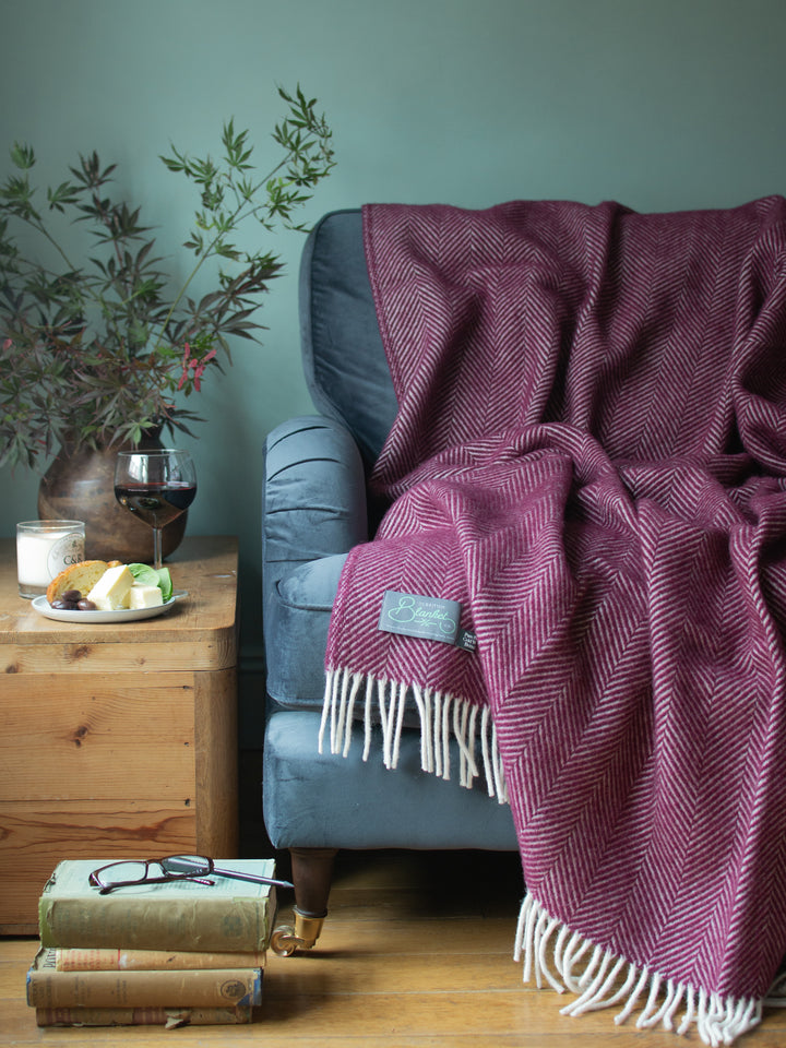A burgundy herringbone wool blanket draped over a blue sofa. 