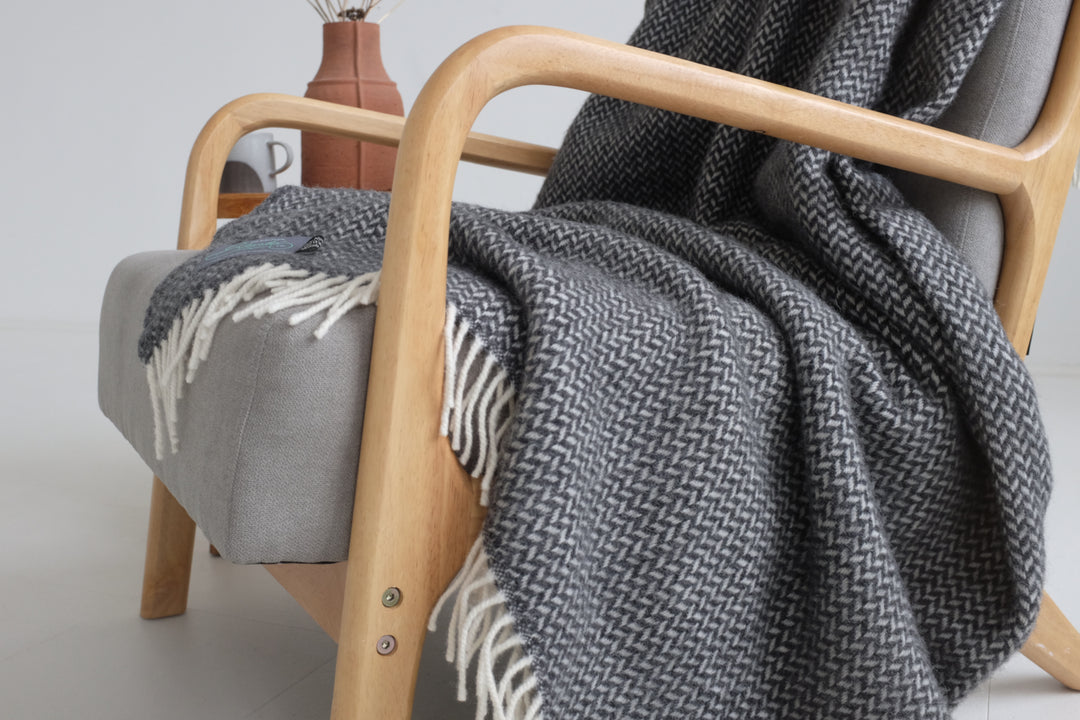 Closeup of large grey herringbone wool blanket draped on lounge chair. 