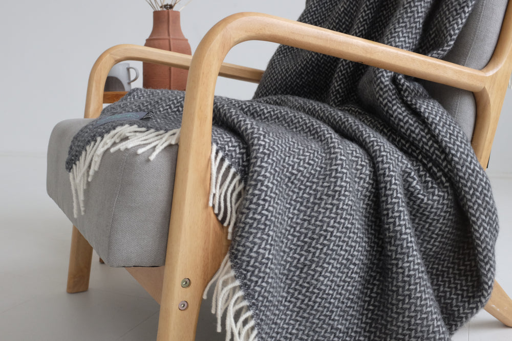 A grey herringbone wool blanket draped over a lounge chair. 