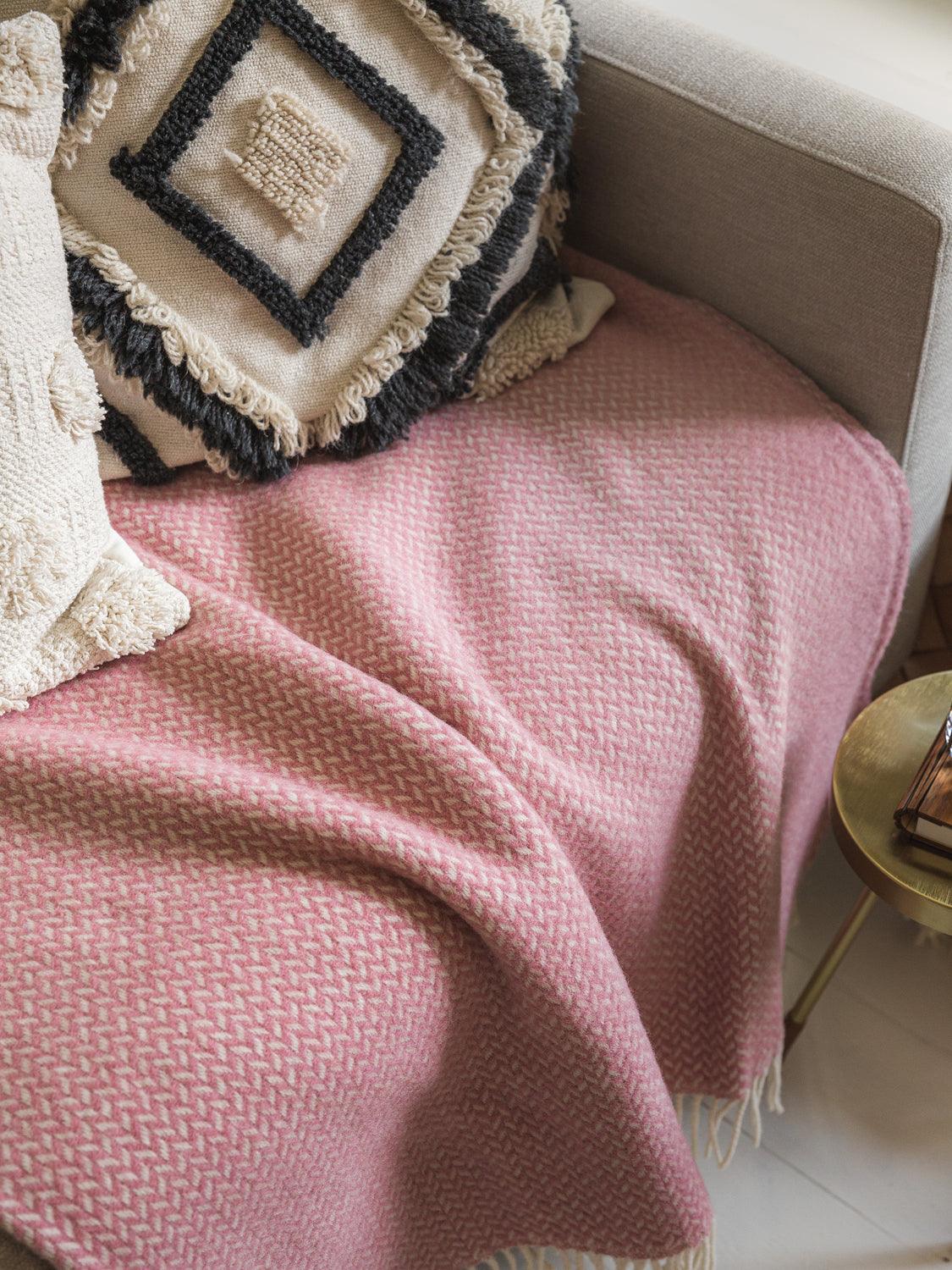Pink herringbone wool blanket draped on sofa underneath two cushions.