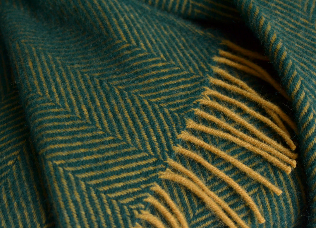 Closeup of a green and yellow herringbone wool blanket with yellow tassels. 