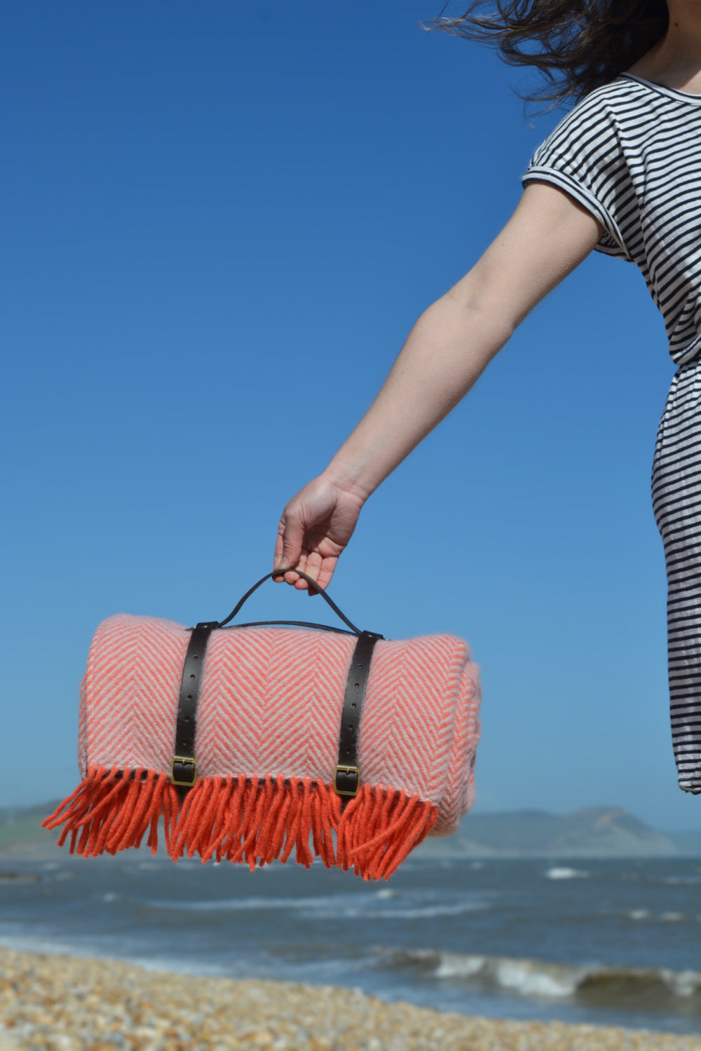 A woman holding a rolled up pink wool picnic rug.