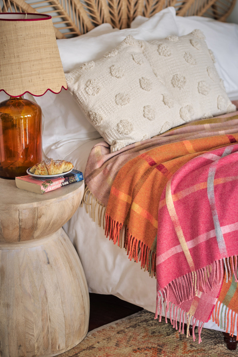 Three Garden Flowers lambswool throws draped over a bed next to a bedside table
