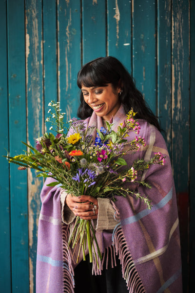 Large purple Garden Flowers blanket wrapped around a woman smiling down at a bouquet of flowers