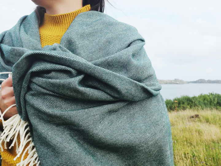 A woman wrapped in a green herringbone wool blanket. 