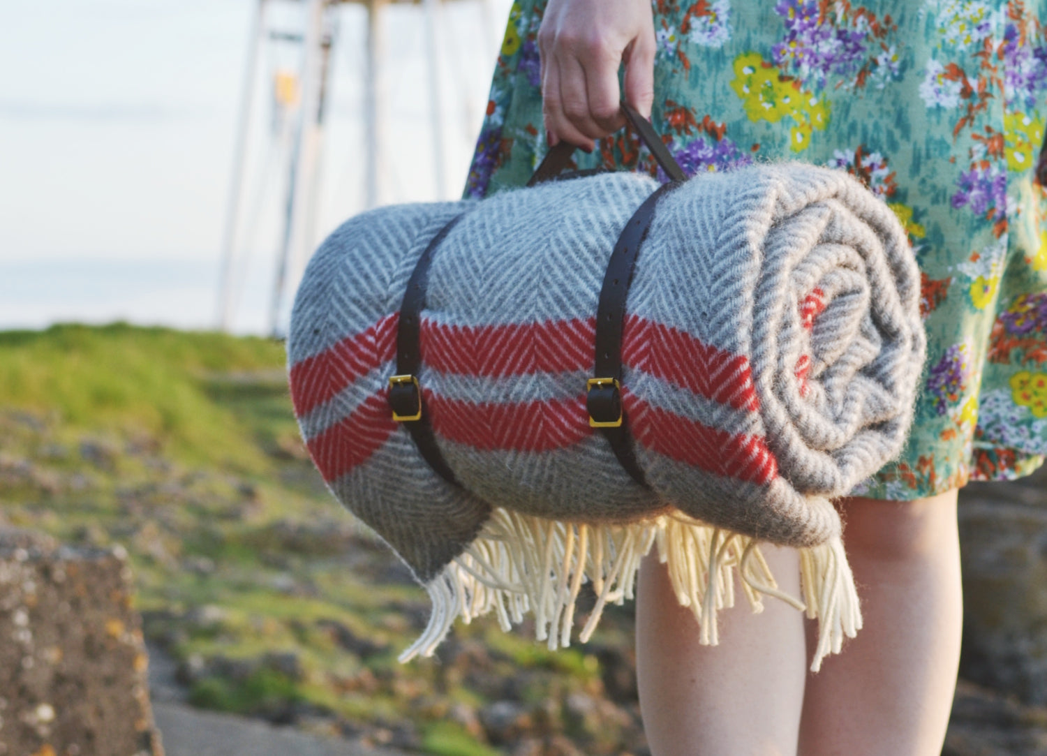 A woman holding the handle of a leather strap carrying a wool picnic blanket