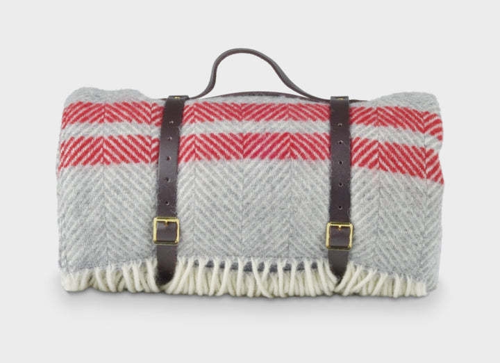 Grey and red wool picnic rug by The British Blanket Company rolled up with leather straps.