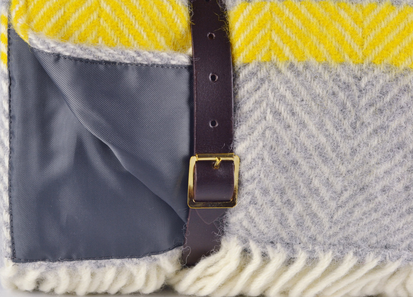 Closeup of leather straps wrapped around a grey and yellow wool picnic rug by The British Blanket Company.