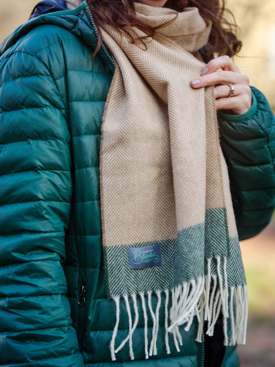 A woman holding a beige and green lambswool scarf wrapped around her neck.