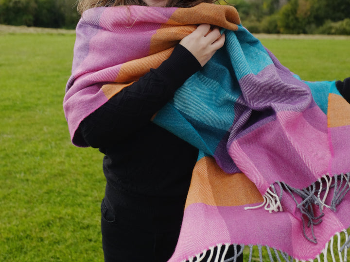 A woman wearing a multicoloured oversized lambswool scarf over her shoulder and around her neck.