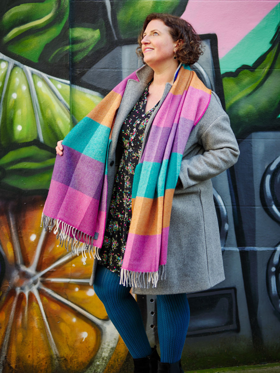 A multicoloured oversized lambswool scarf draped over a woman's shoulders.