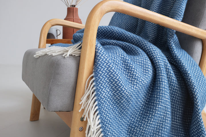 Closeup of a large blue herringbone wool blanket draped over a grey lounge chair