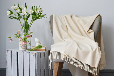 Extra large cream merino herringbone wool blanket draped over a lounge chair