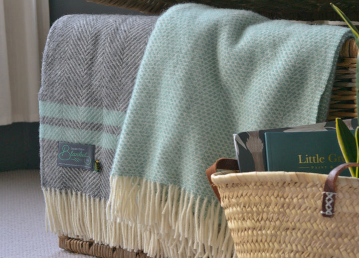 Large green and grey wool blankets hanging out of a wicker basket