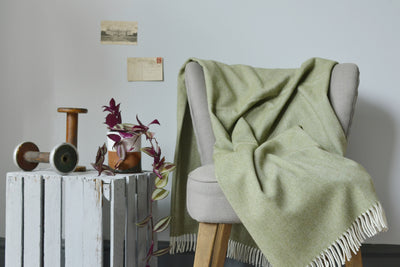 Large green merino herringbone wool blanket draped over a lounge chair. 