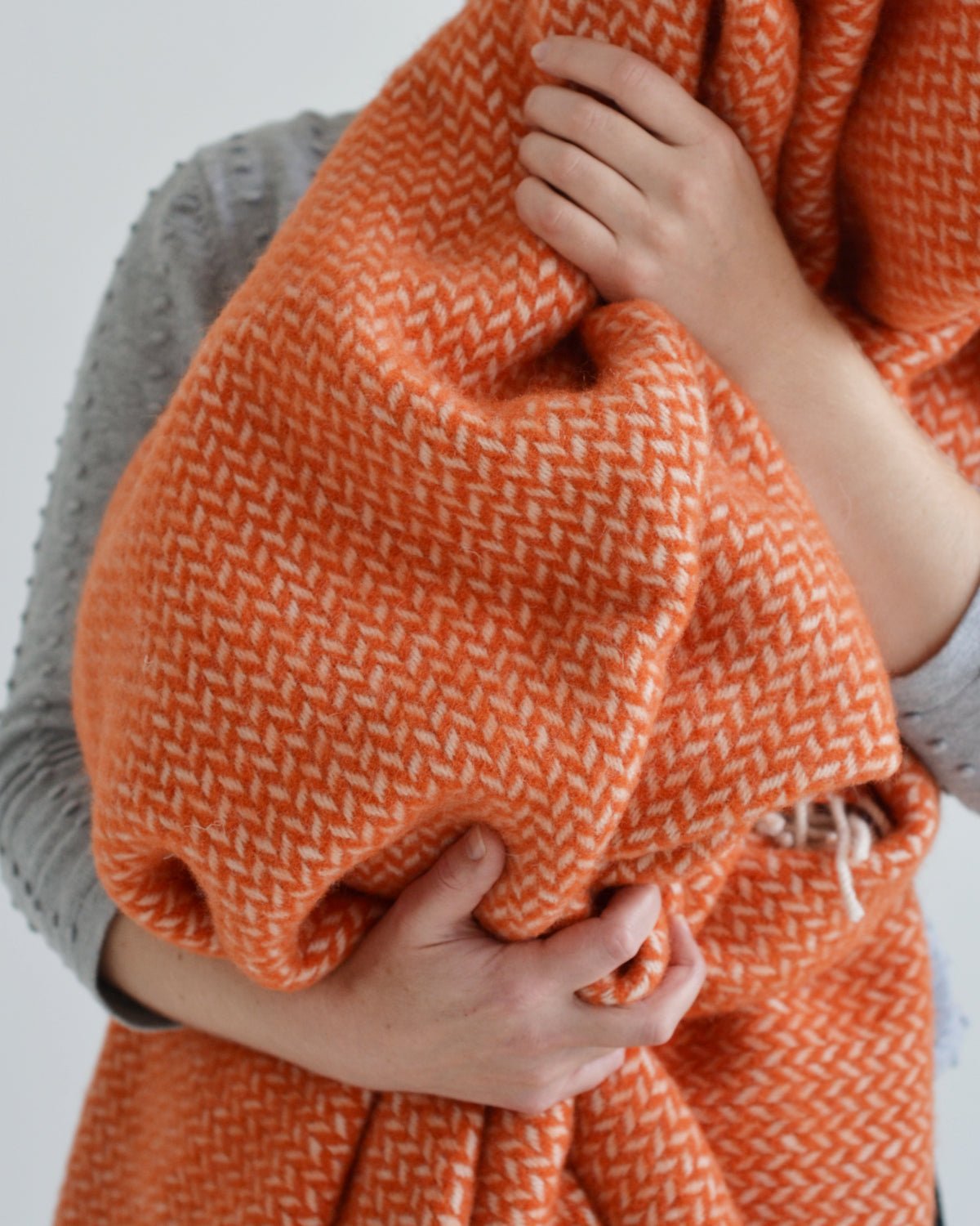 A woman holding an orange herringbone wool blanket in her arms