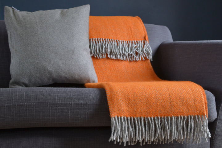 Large orange and grey herringbone wool blanket draped over a sofa next to a cushion