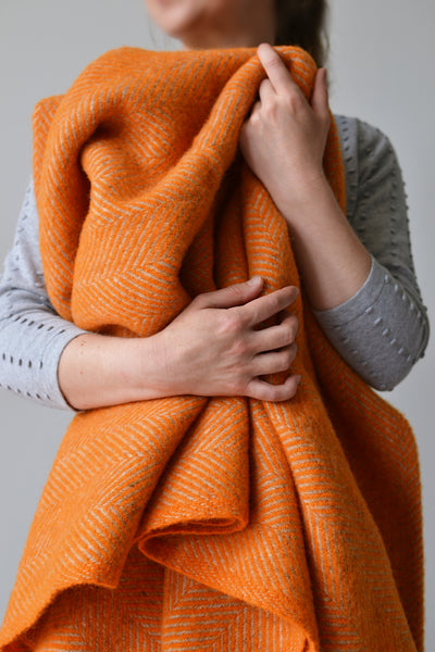 A woman holding an orange and grey herringbone wool blanket in her arms