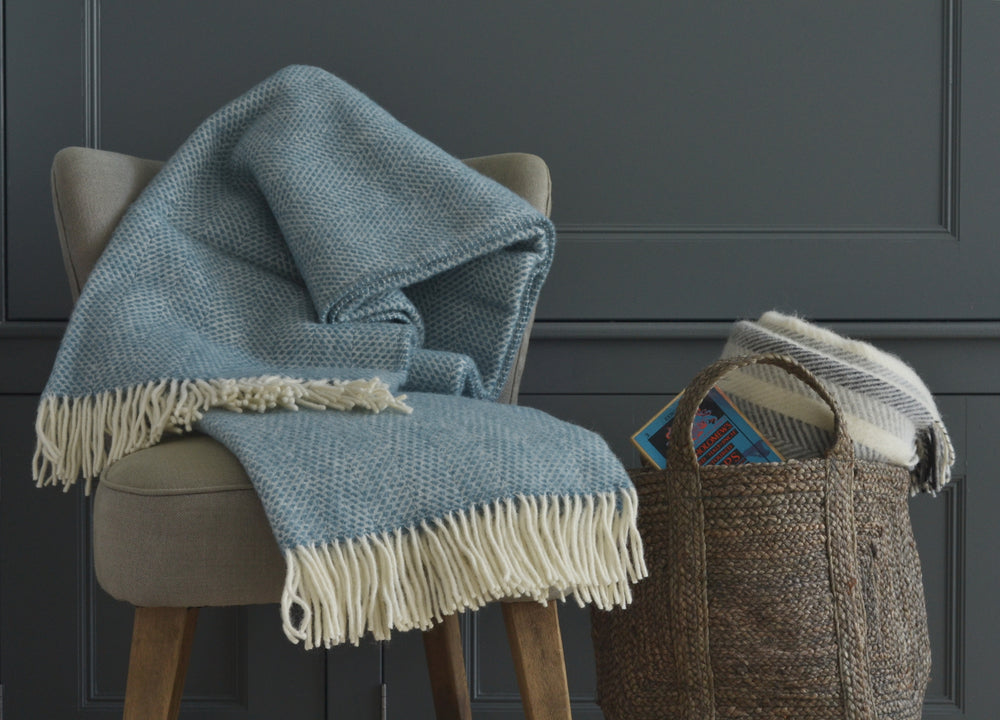 Large blue beehive wool blanket draped over a lounge chair on the left. A rolled up wool blanket inside a basket is on the right