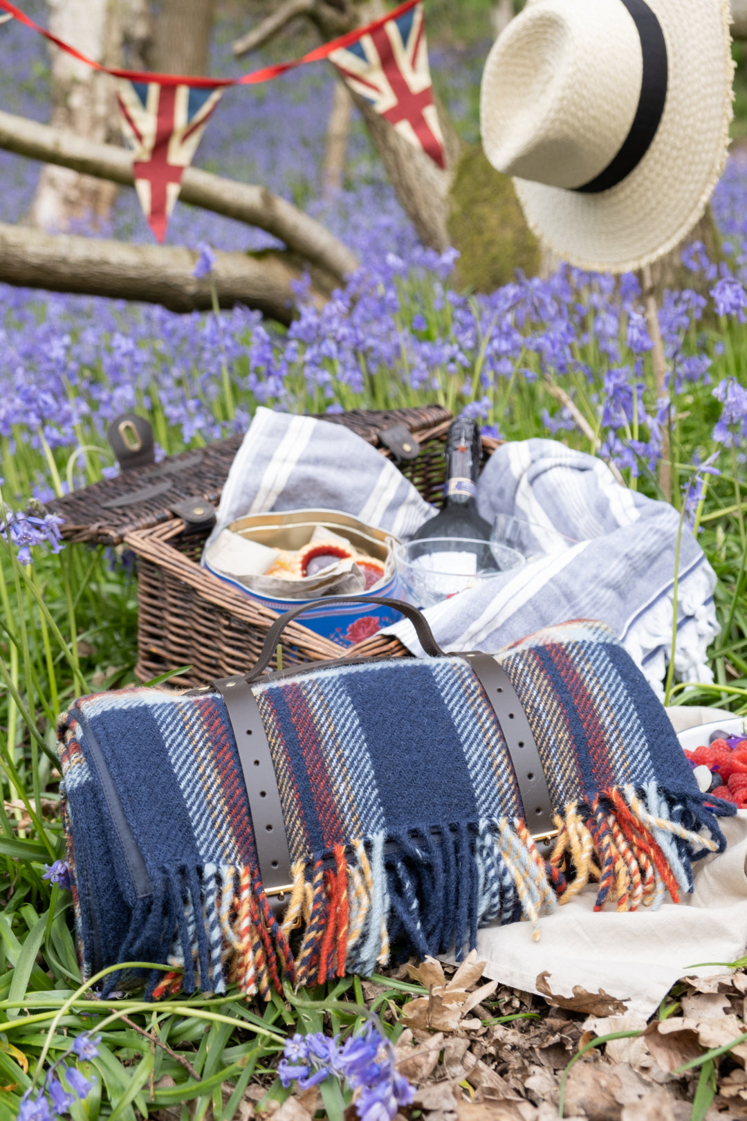 Rolled up wool picnic blanket on grass with a picnic basket behind it. 