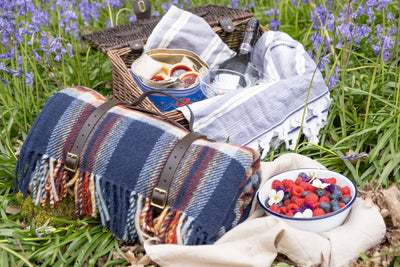 Rolled up picnic rug placed on grass alongside a picnic basket and a bowl of berries. 