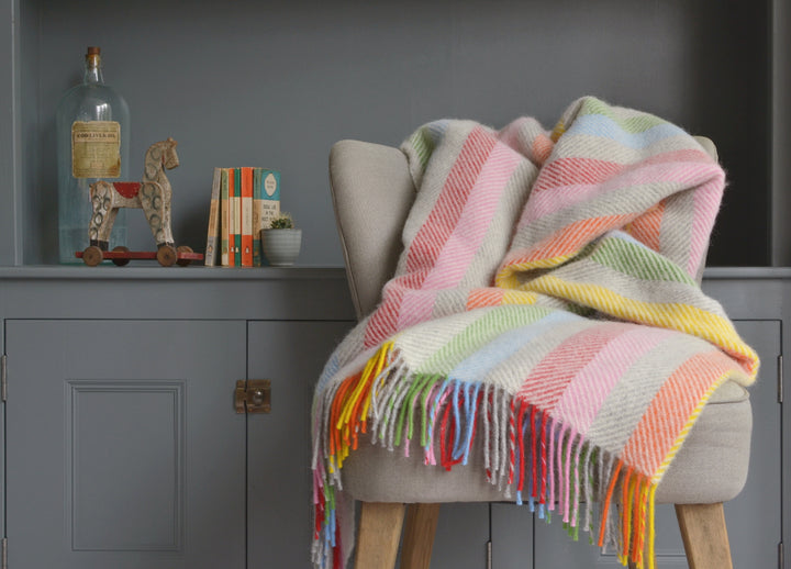 Large rainbow stripe herringbone wool blanket draped over a lounge chair