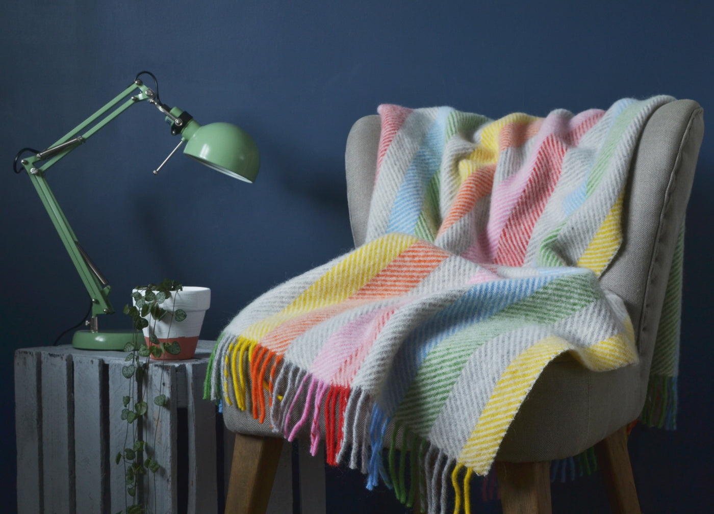 Rainbow stripe herringbone wool blanket draped over a lounge chair