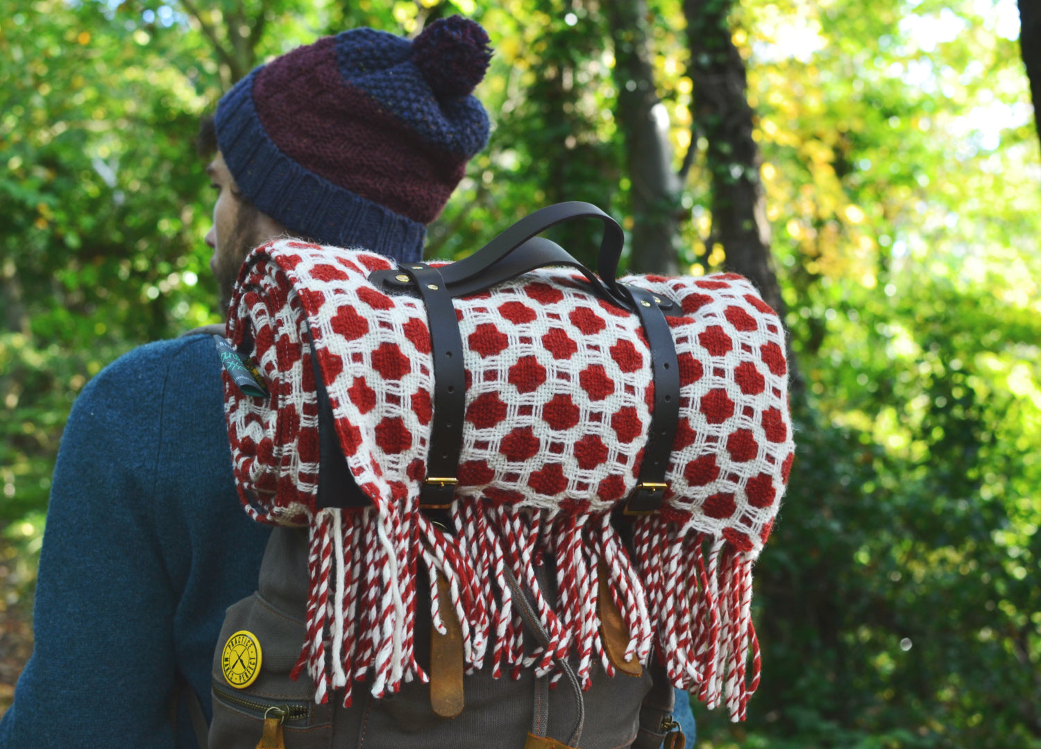 A wool picnic blanket rolled up with leather straps being carried on a man's backpack