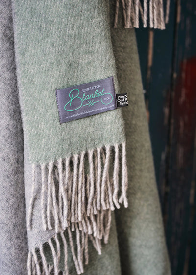 Corner of a green and grey reversible wool throw blanket by The British Blanket Company