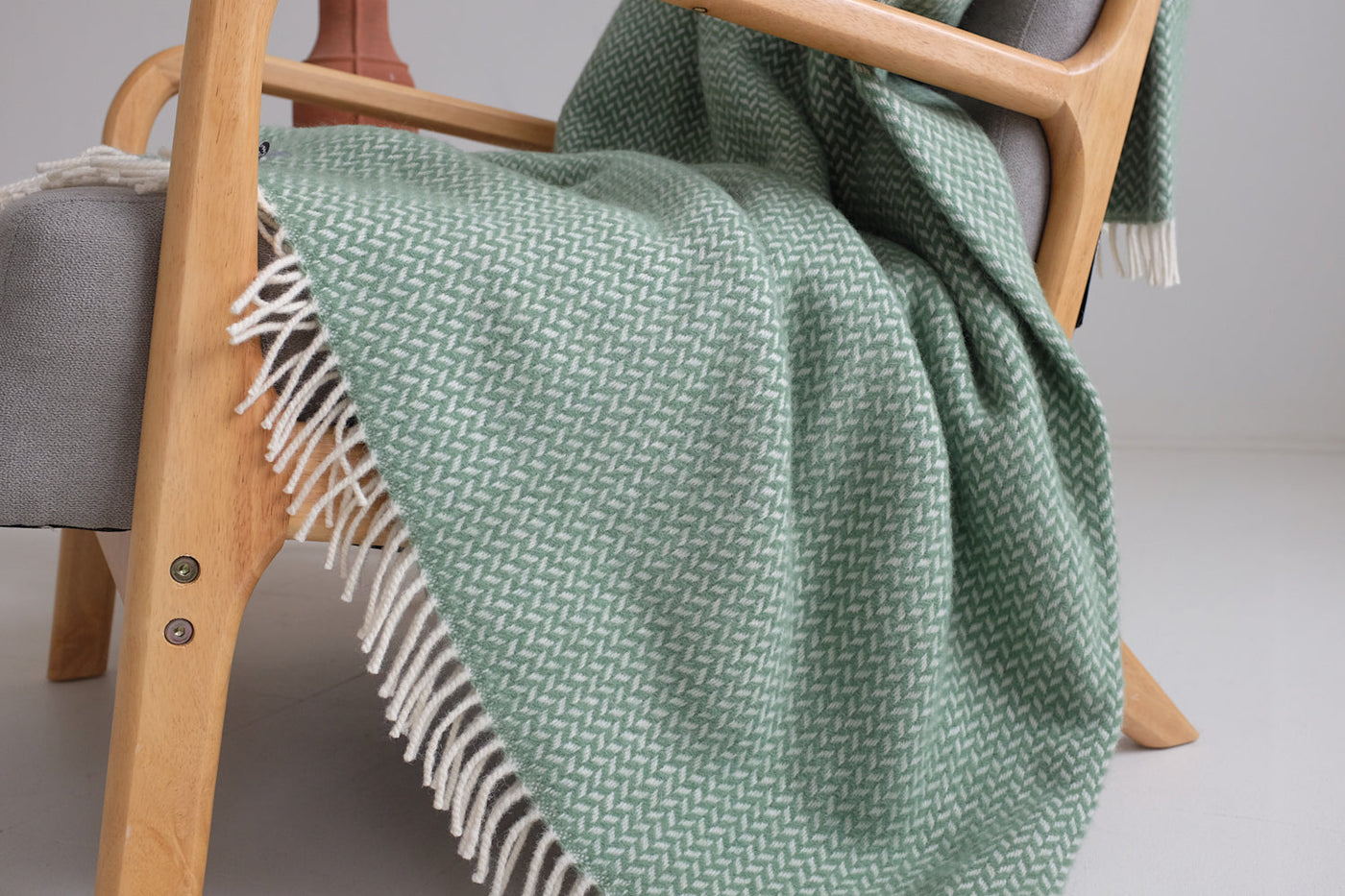Extra large green herringbone wool blanket draping off the edge of a lounge chair