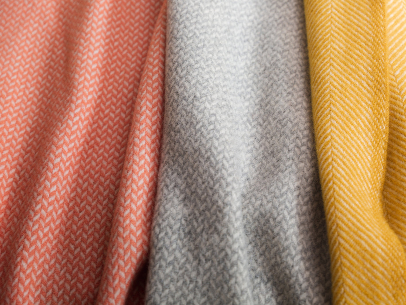 Three herringbone wool blankets in orange, grey, and yellow.