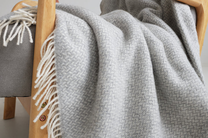 Closeup of a silver grey herringbone wool blanket draping off the side of a lounge chair