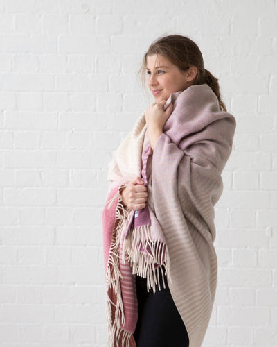 A woman holding a large pink ombre merino wool blanket wrapped around her body