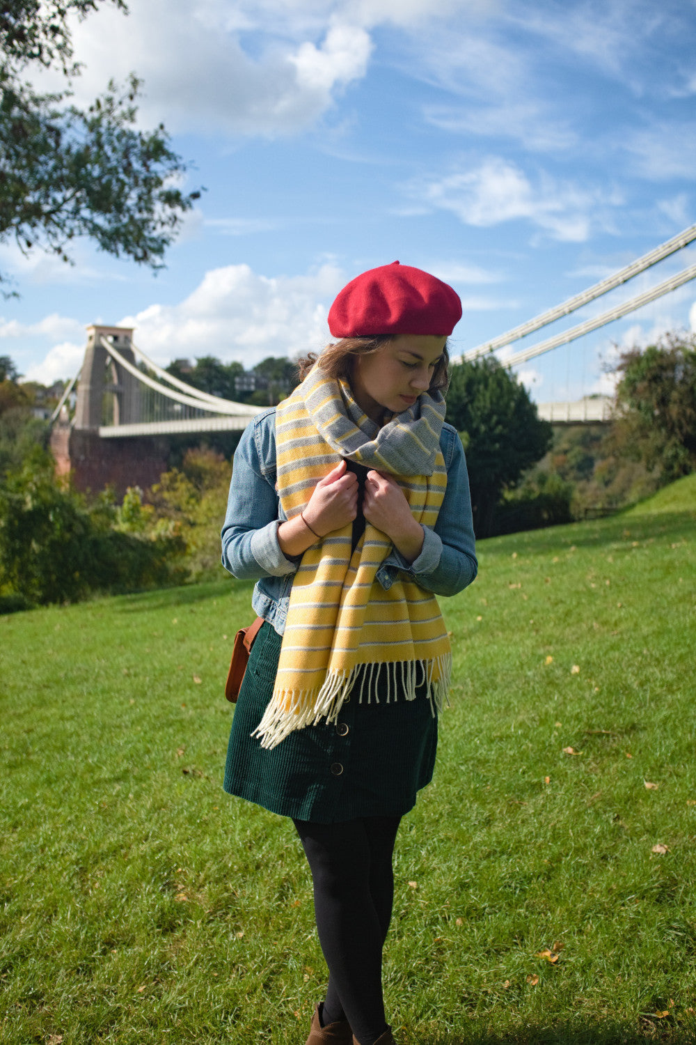 A woman looking down while holding a yellow and grey blanket scarf wrapped around her neck