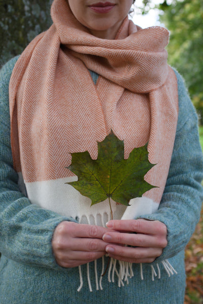A woman wearing an orange and cream lambswool scarf holding a green leaf. 