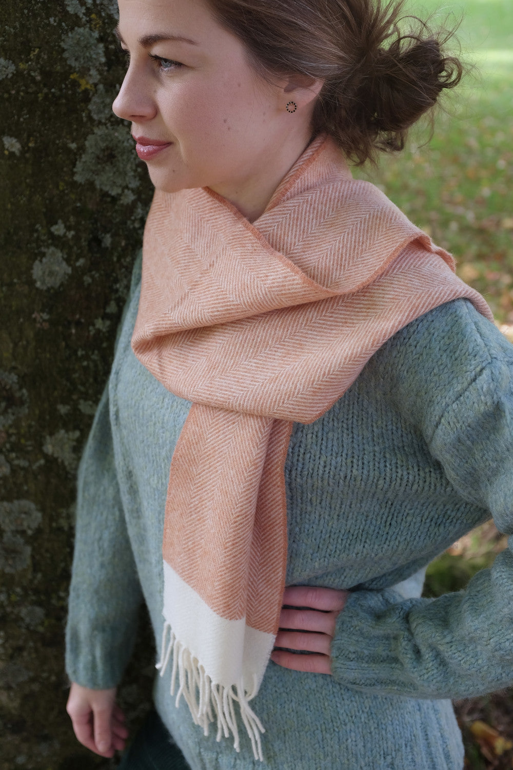 A woman wearing an orange and cream lambswool scarf by The British Blanket Company. 