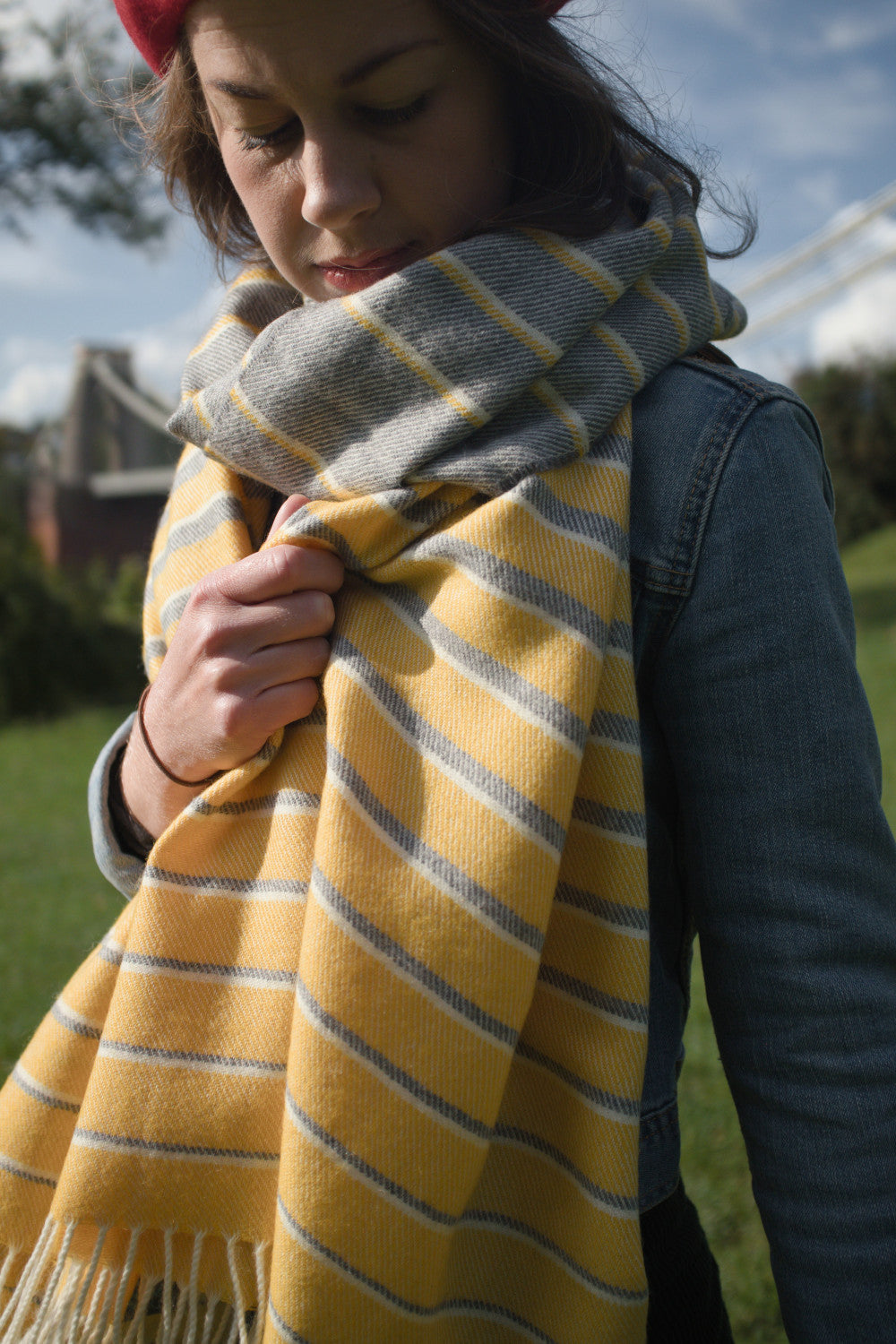 A woman holding a grey and yellow oversized blanket scarf wrapped around her neck