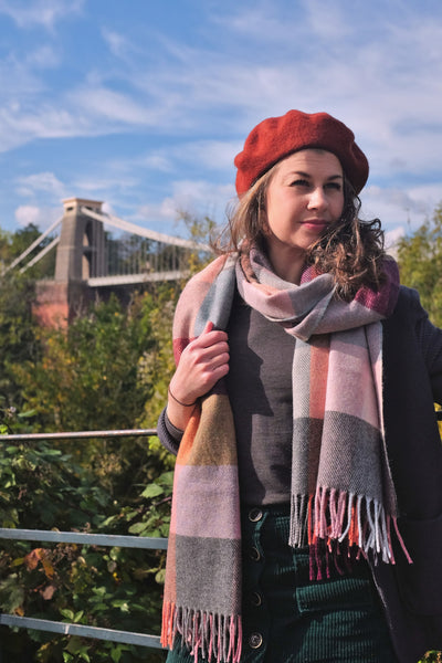 A woman wearing an oversized purple and yellow wool scarf with the Clifton Suspension Bridge in the background.