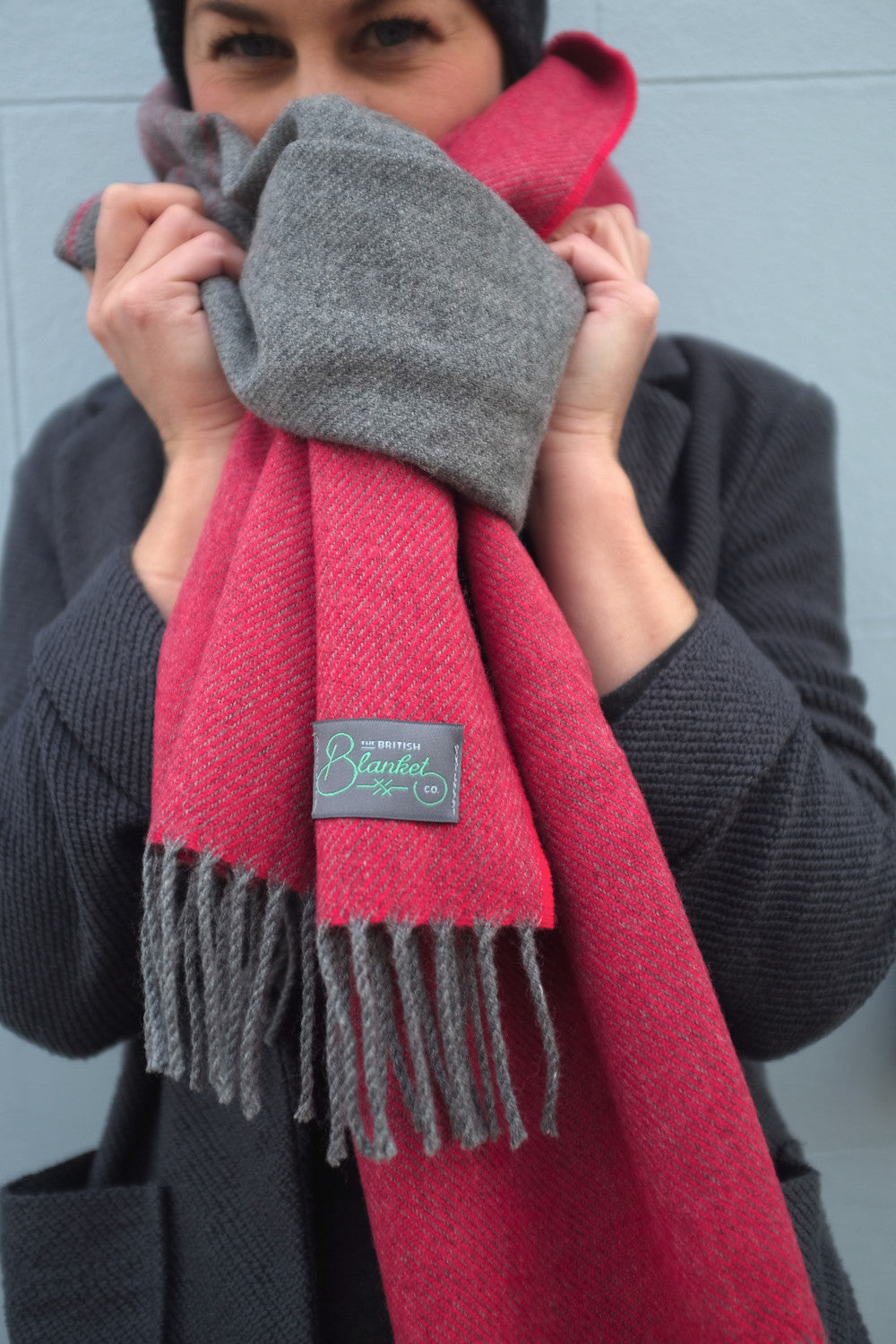 A woman peaking through a red and grey oversized blanket scarf wrapped around her neck