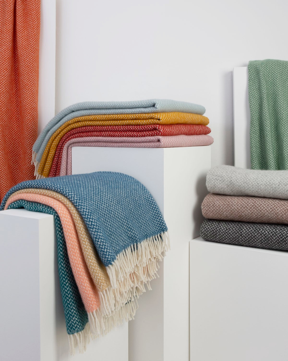 Folded wool blankets in various colours stacked on display plinths.