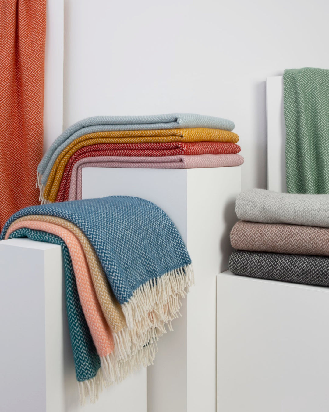 Several folded wool blankets in various colours stacked on display plinths