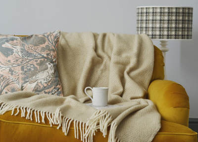 Large beige beehive wool blanket draped over a yellow sofa. A mug is set in the middle of the blanket, while a cushion is on the left