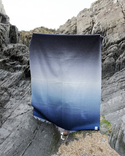 A person holding up a large blue ombre merino wool throw