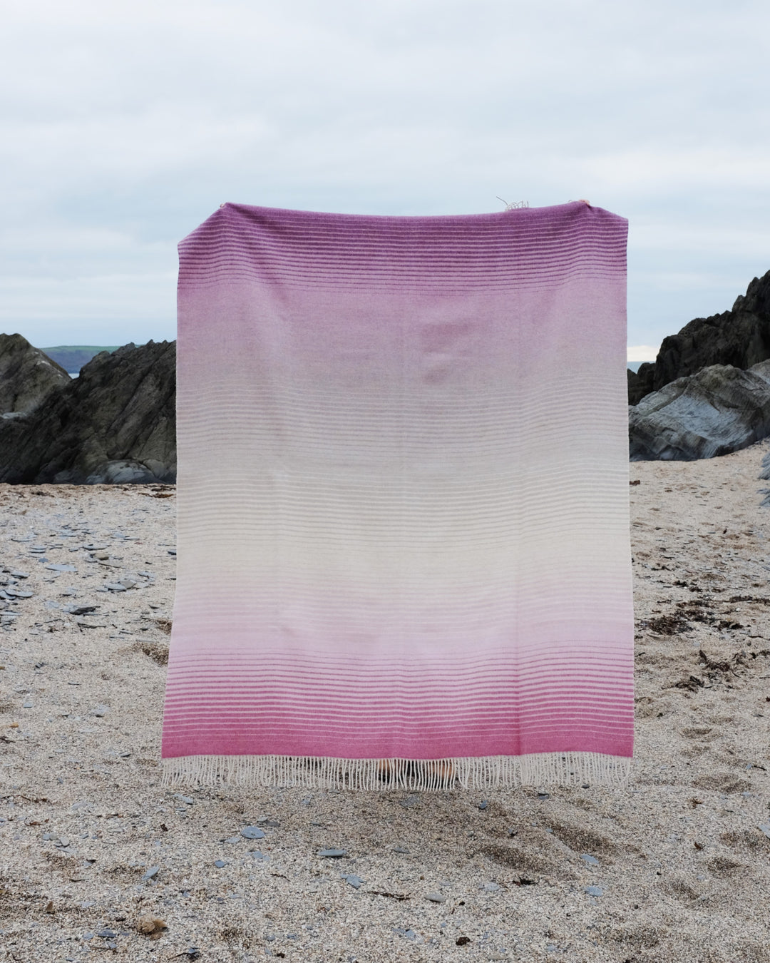 A person holding up a large pink ombre merino wool throw